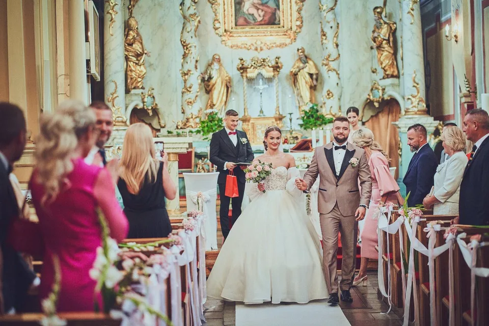 Para młoda idzie nawą między gośćmi